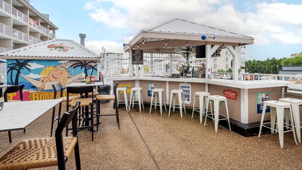 A beachside bar area with outdoor seating, a mural, and a sign advertising a happy hour. - Quality Inn & Suites Ocean City Fenwick (Ocean City)
