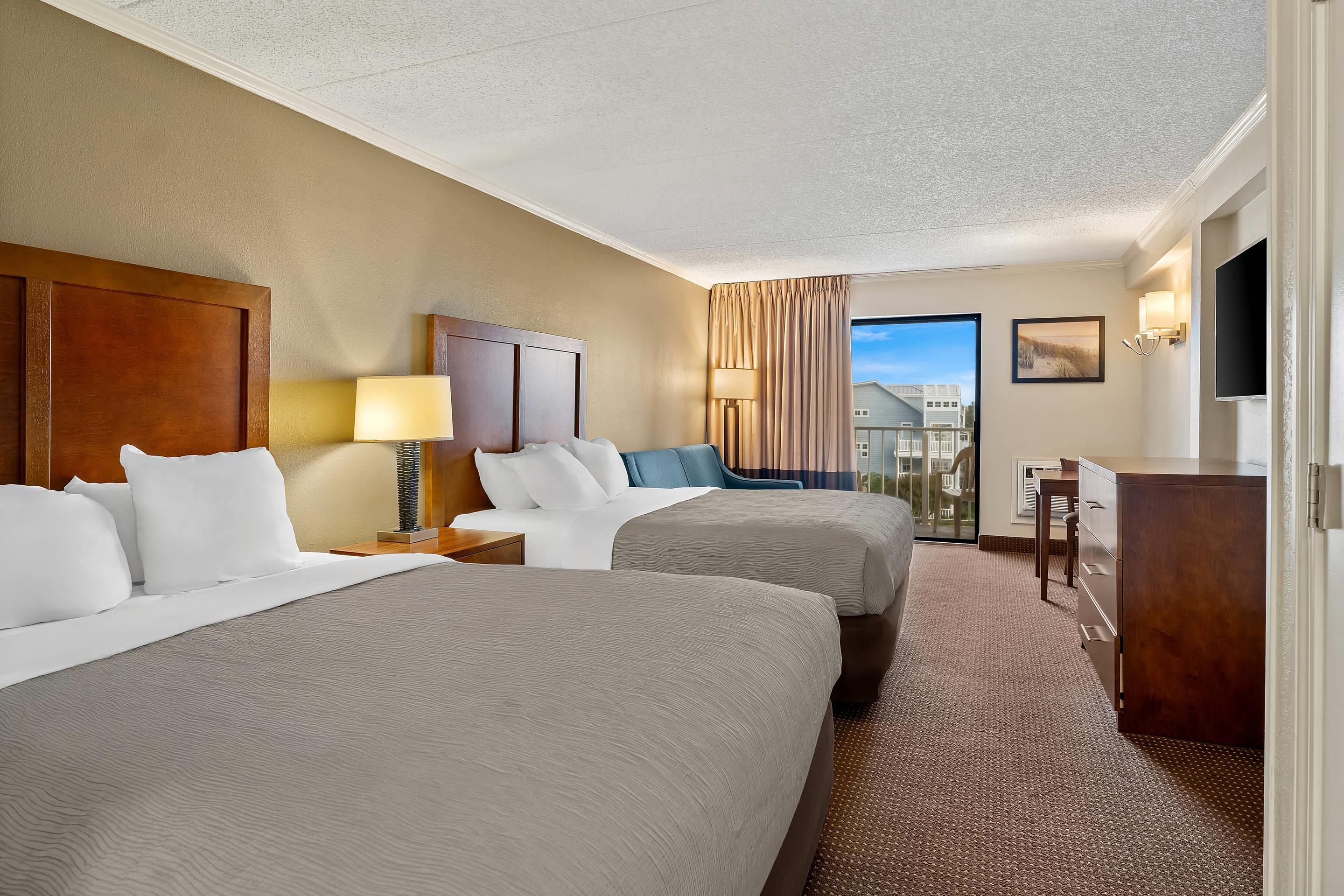 A hotel room with two beds, a desk, a chair, a lamp, and a TV.