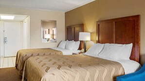A hotel room with two beds, a wooden headboard, a nightstand with a lamp, and a door. - Quality Inn & Suites Ocean City Fenwick (Ocean City)