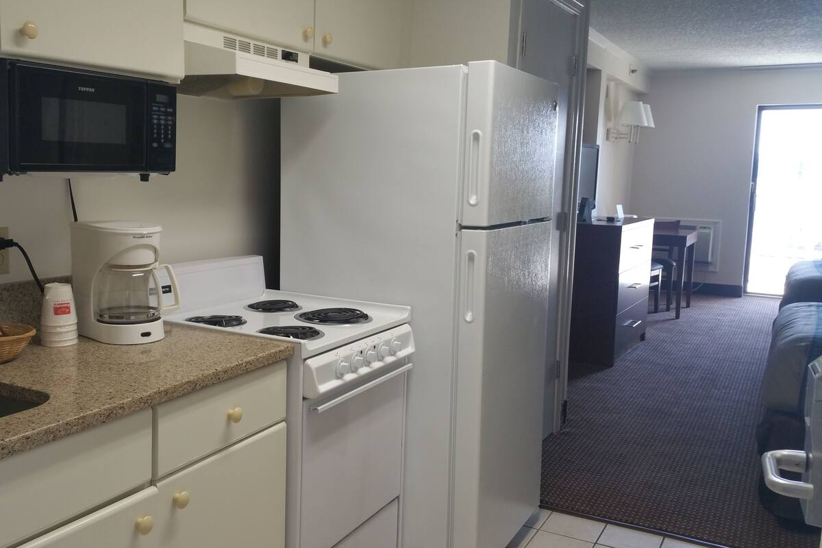 A compact kitchen with a microwave, stove, and refrigerator. There is a coffee maker on the counter and a sink with a faucet.