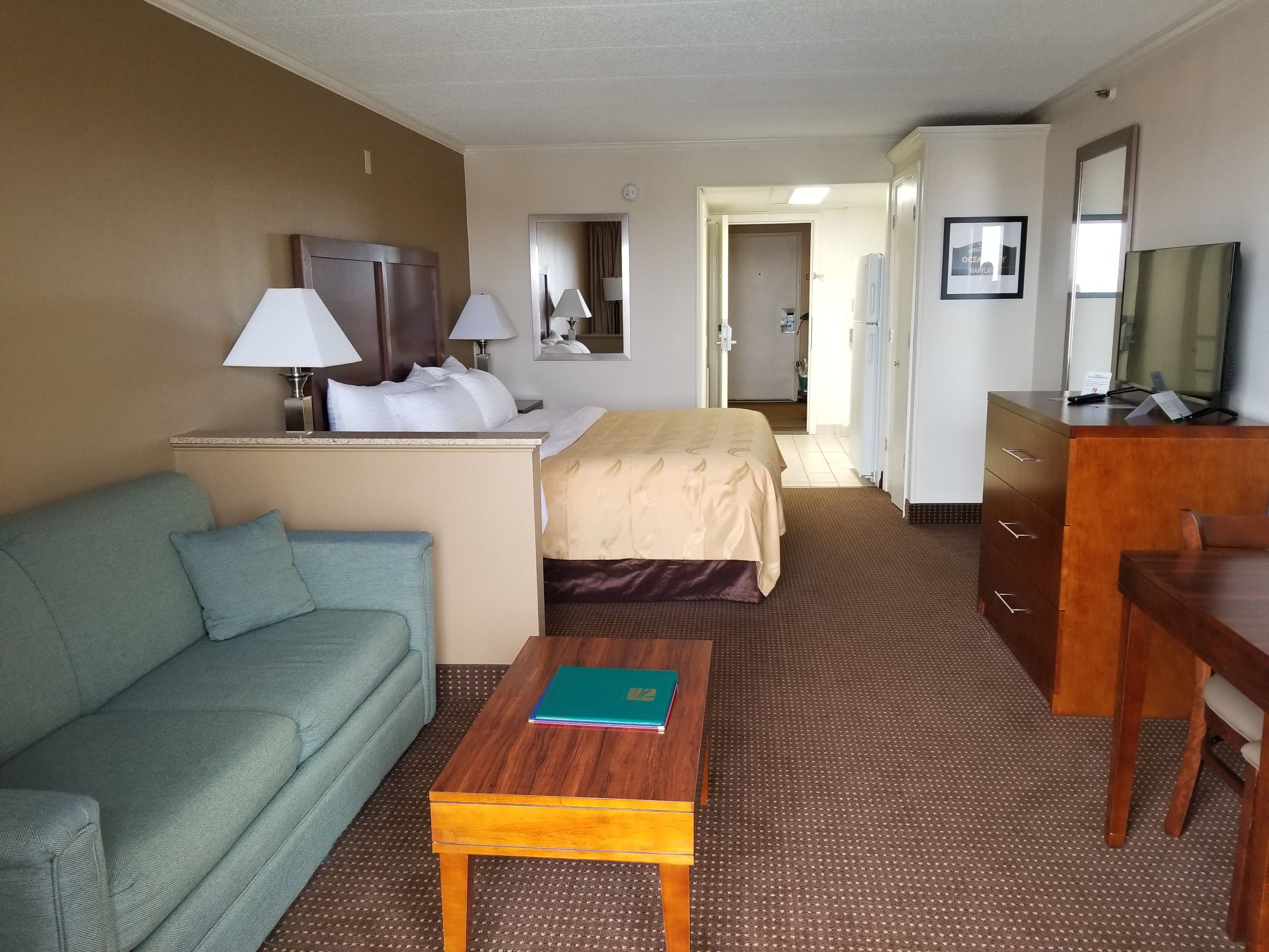 A hotel room with a bed, a sofa, a desk, a TV, and a mirror.