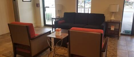 A lobby with a sofa, two armchairs, a small table, a lamp, and a television.