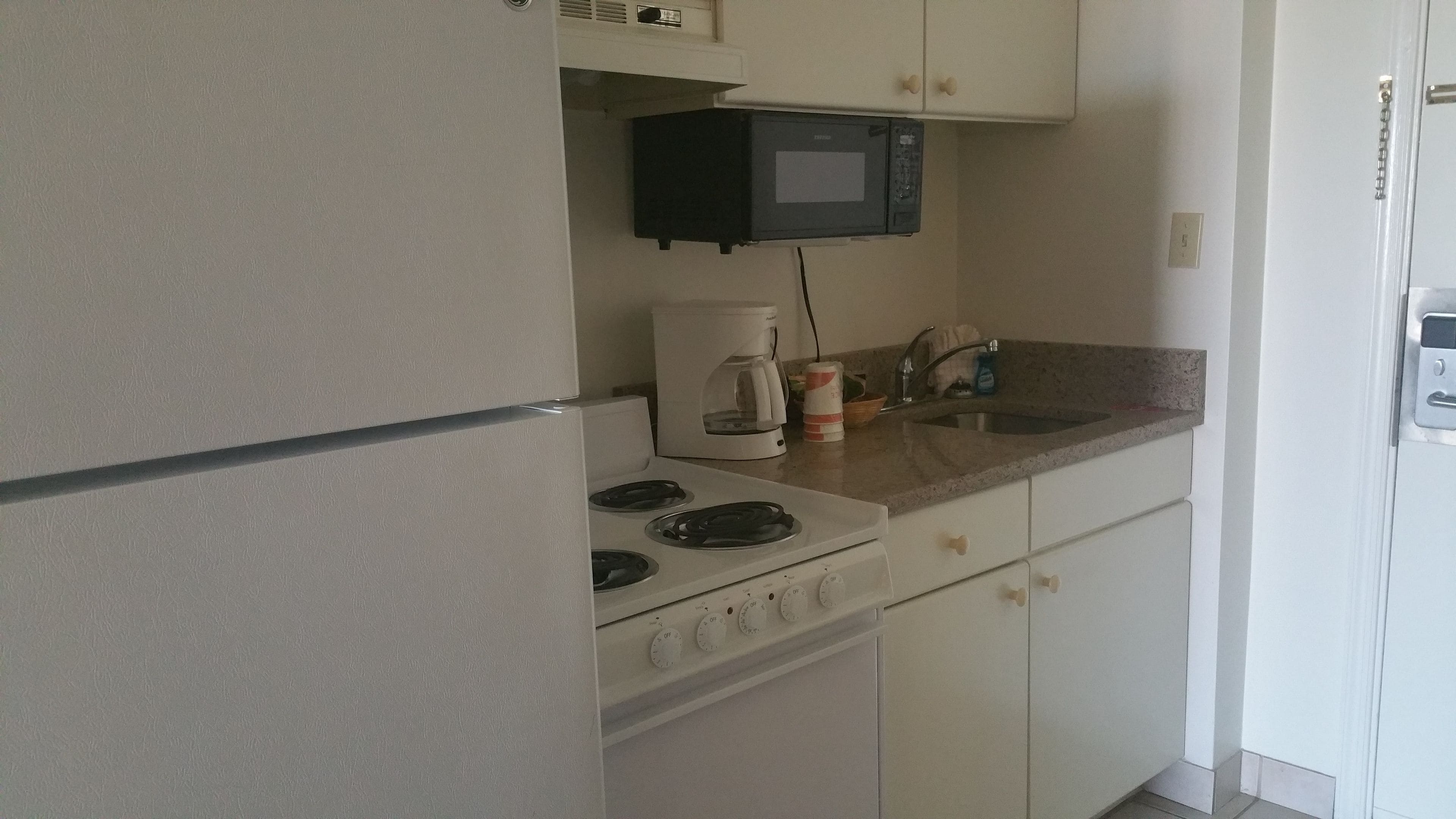 A compact kitchen with a refrigerator, stove, microwave, and sink.