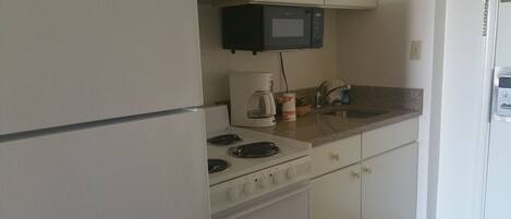 A compact kitchen with a refrigerator, stove, microwave, and sink.