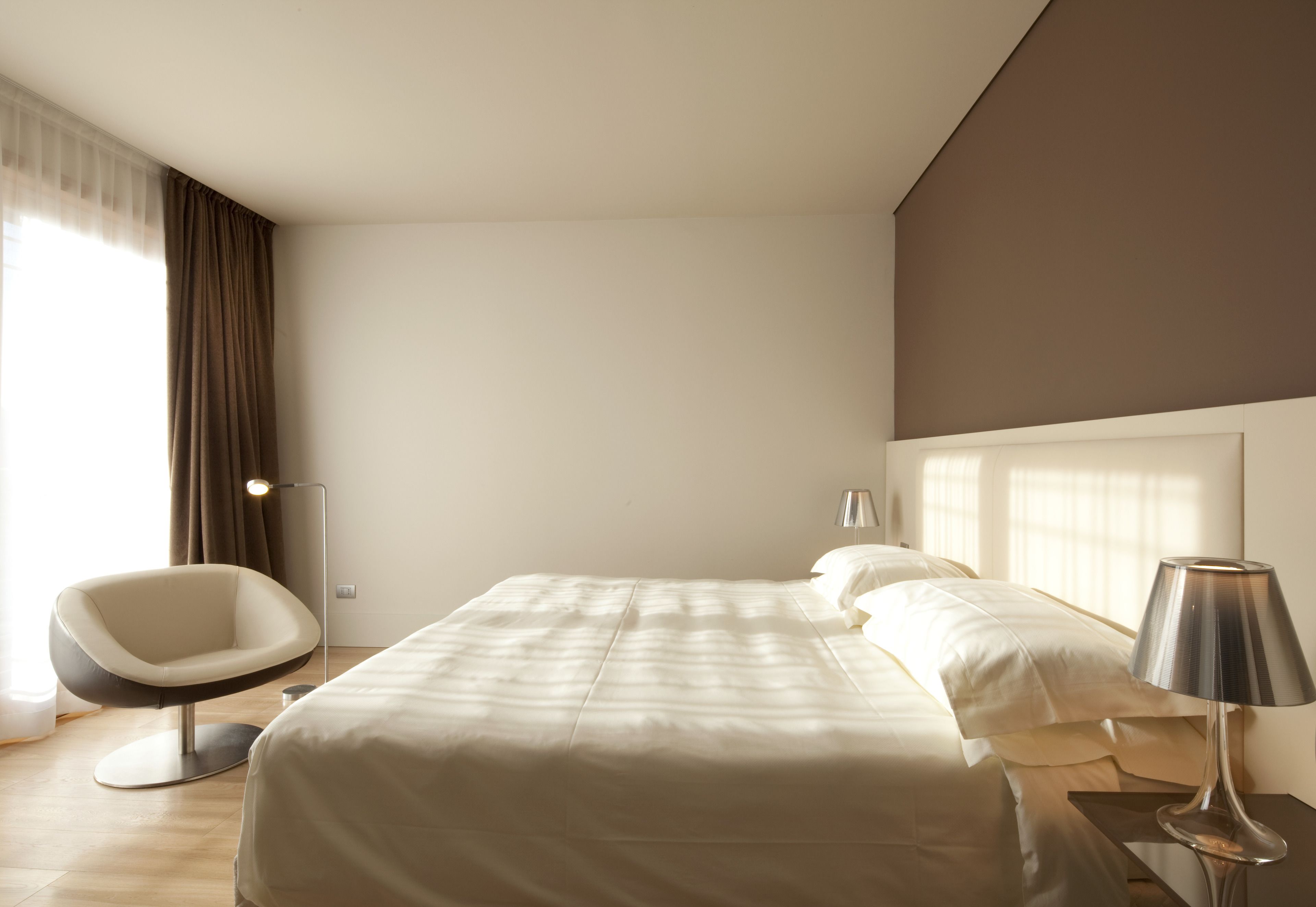 Een moderne hotelkamer met een groot bed, een stoel, een lamp en een raam met gordijnen.