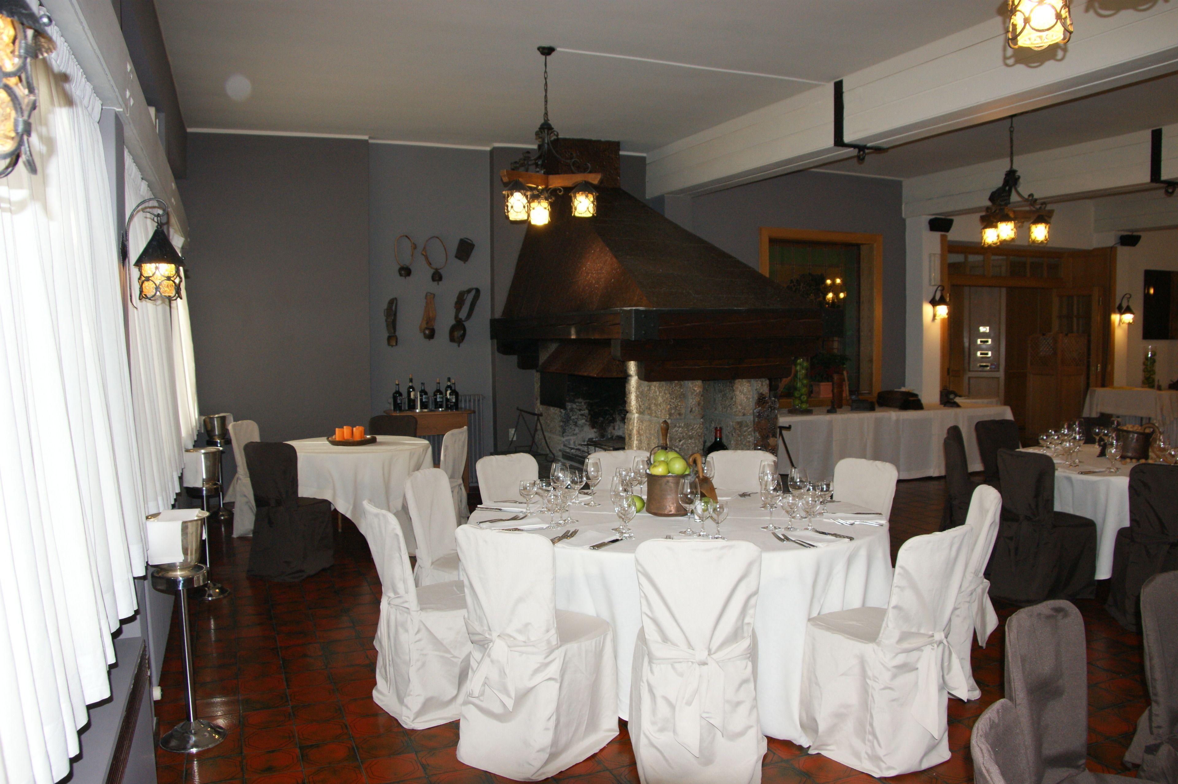A dining area with round tables set for a meal, white chairs, and a stone fireplace.