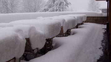 Un espacio exterior cubierto de nieve con estructuras de madera, posiblemente un patio o terraza, rodeado de árboles cargados de nieve.