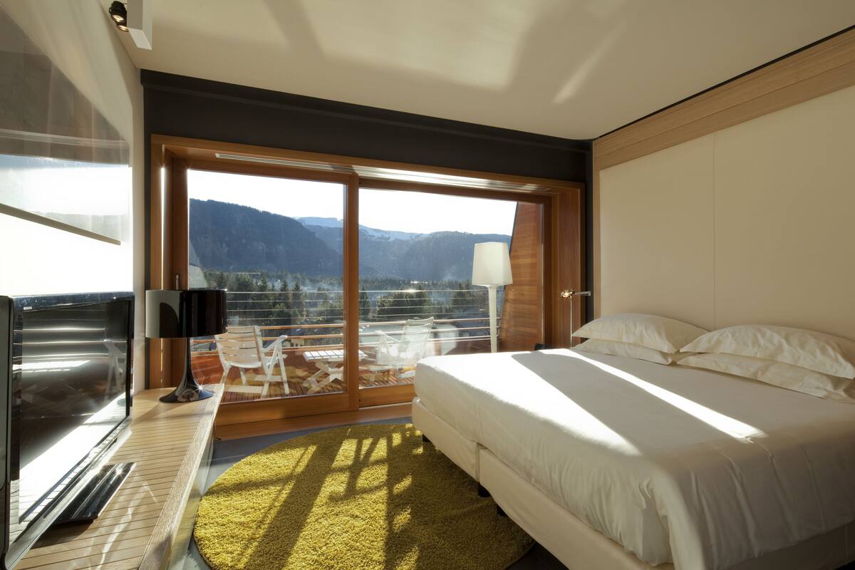 Una habitación de hotel moderna con una cama grande, un televisor y un balcón con vistas a la montaña.