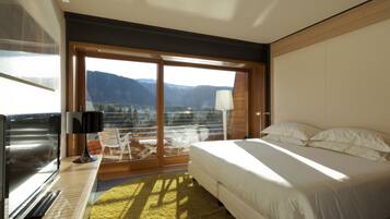 Quarto de hotel moderno com uma cama grande, TV e varanda com vista para as montanhas.