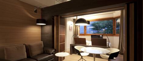 A modern living room with a leather sofa, a round dining table with chairs, a cowhide rug, and a view of the outdoors through a window.