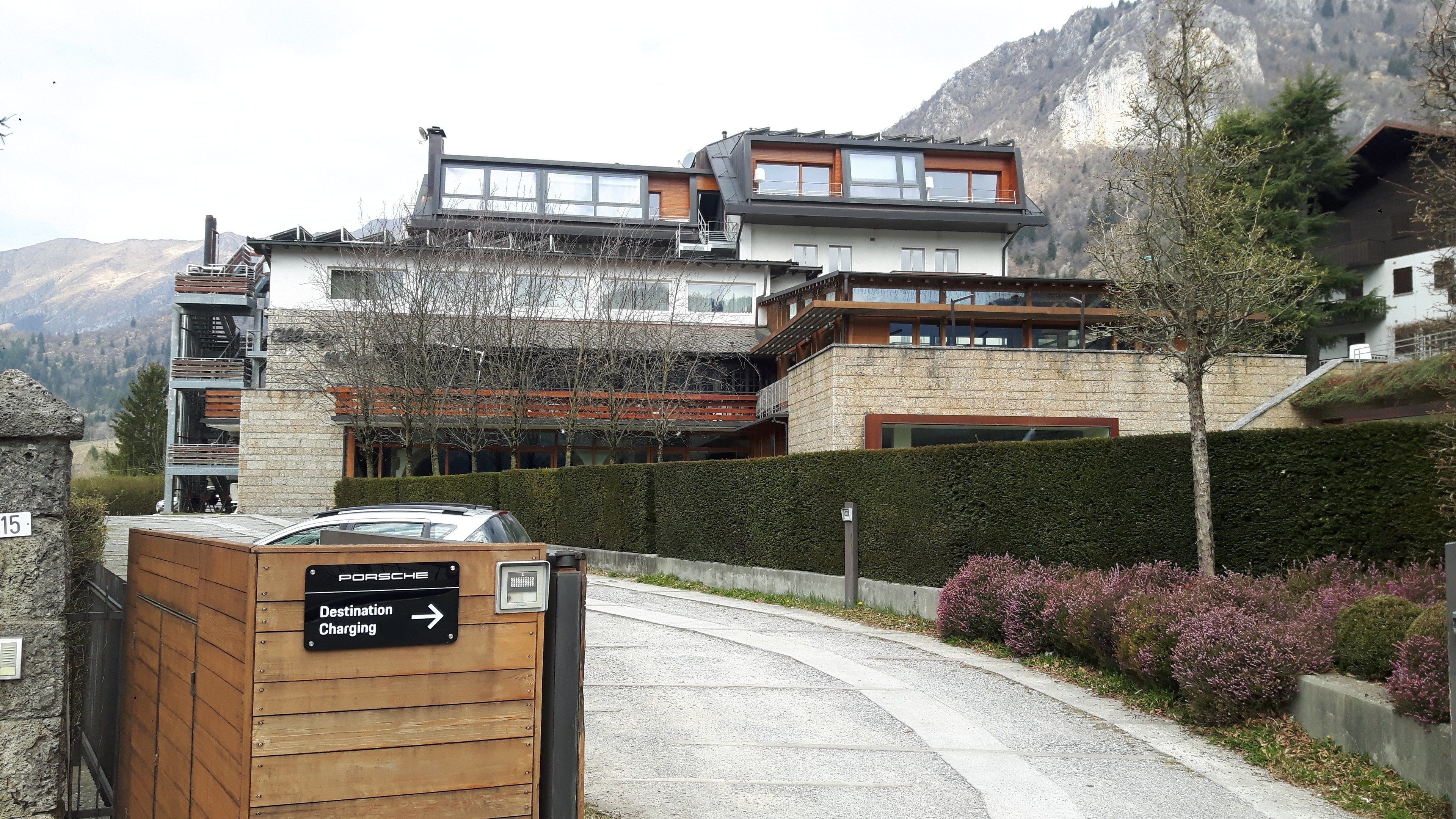A modern building with a wooden facade, a sign indicating destination charging, and a view of mountains in the background.