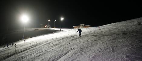 Pista nevada con iluminación artificial y una persona esquiando.