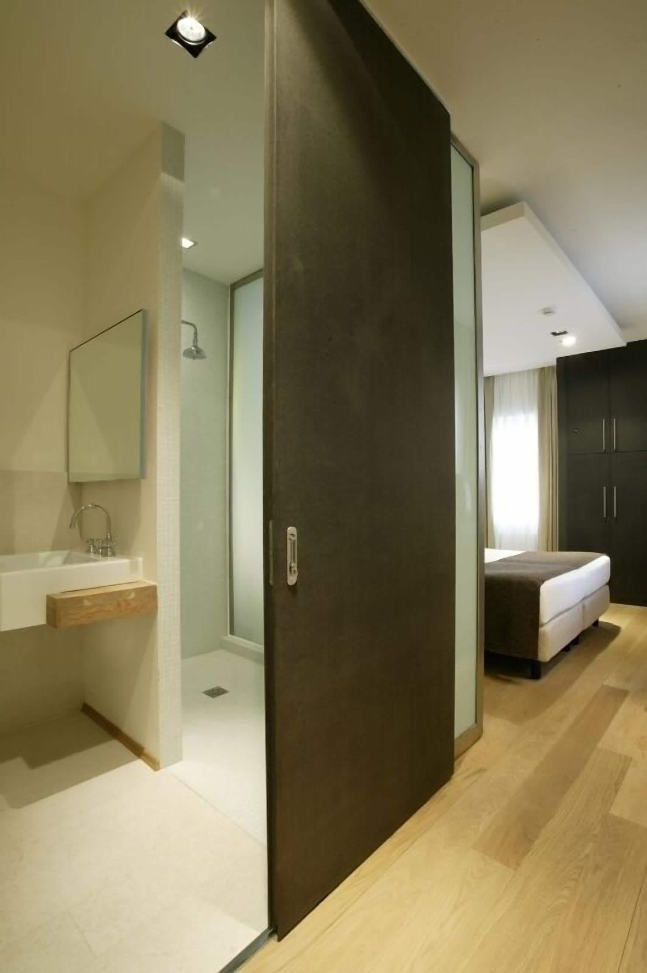 A modern bathroom with a glass shower enclosure, a sink with a mirror, and a wooden shelf.