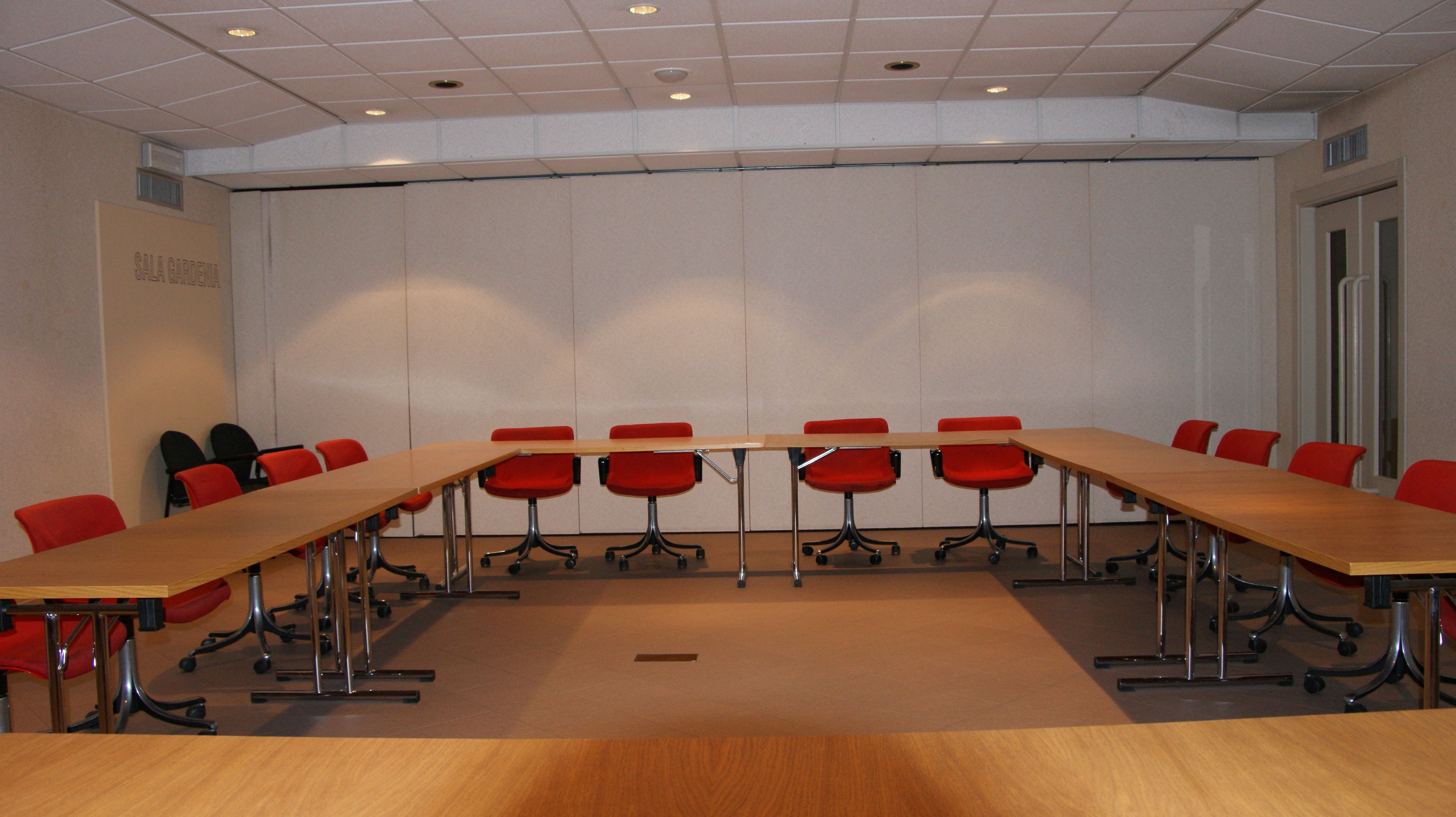 A conference room with a long table and red chairs, a whiteboard, and a door on the right.
