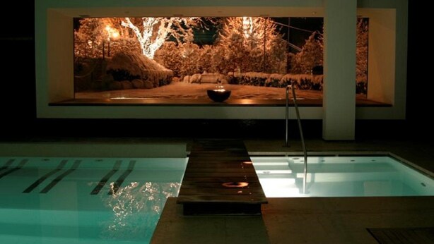 Una piscina amb terrassa de fusta i una pantalla gran il·luminada que mostra una escena natural.