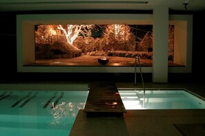 Una piscina con cubierta de madera y una gran pantalla iluminada que muestra una escena natural.
