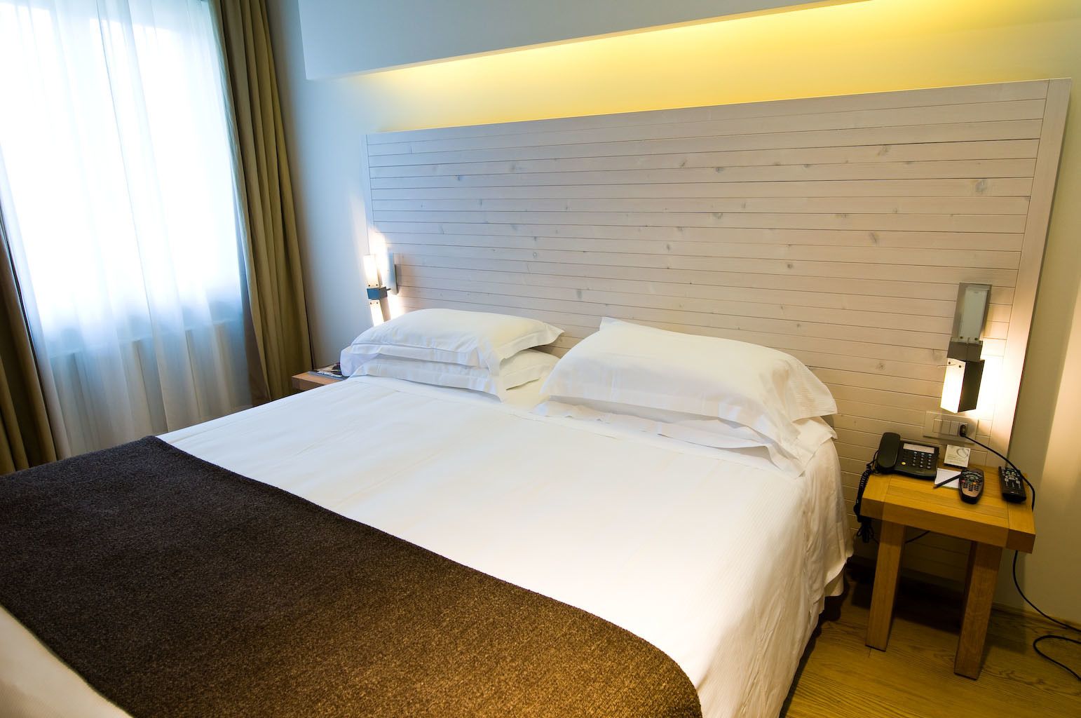 Een hotelkamer met een groot bed, een houten hoofdbord, een nachtkastje met een telefoon en een lamp.