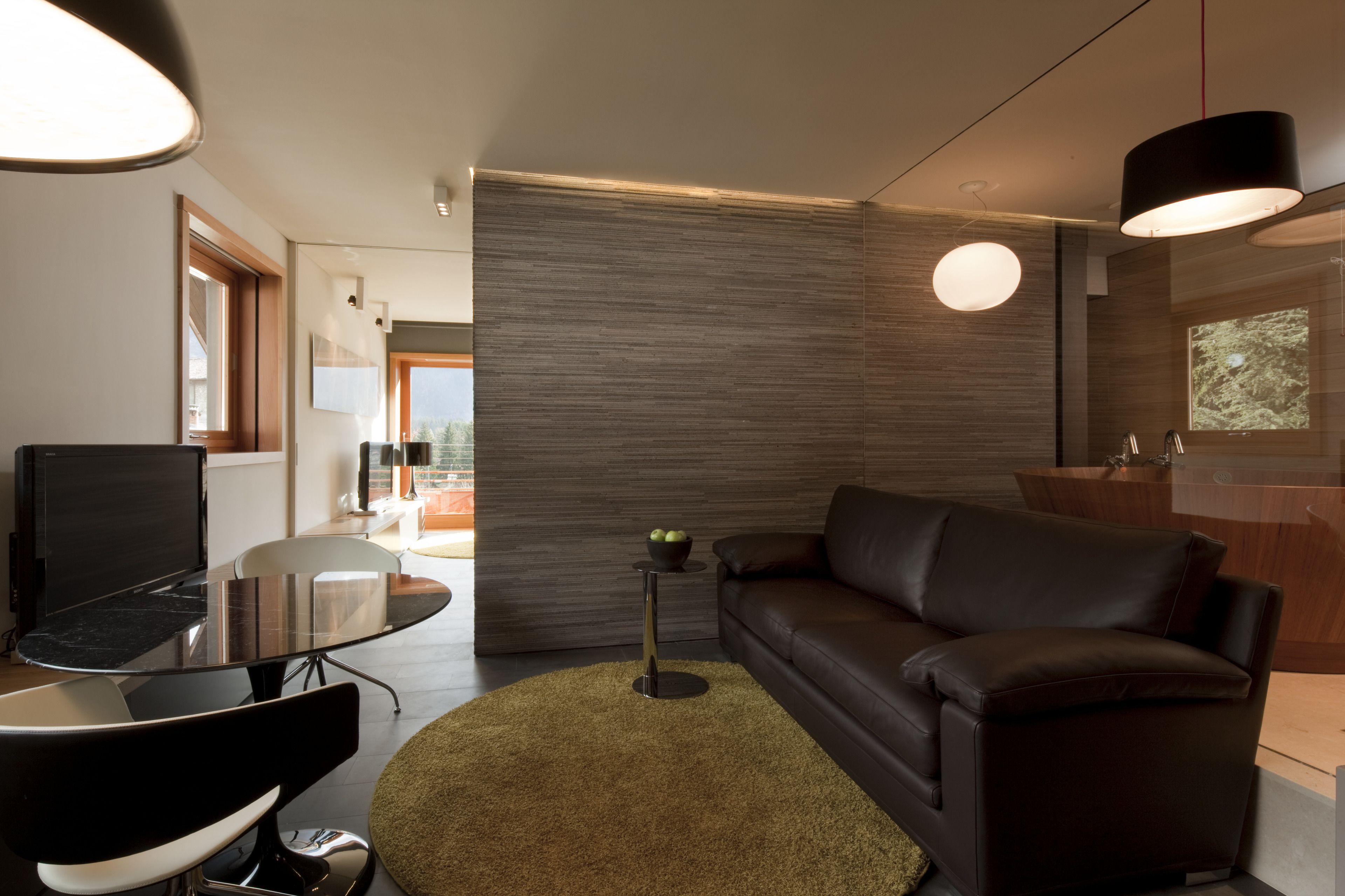 A modern living room with a glass table, a leather sofa, and a round rug.