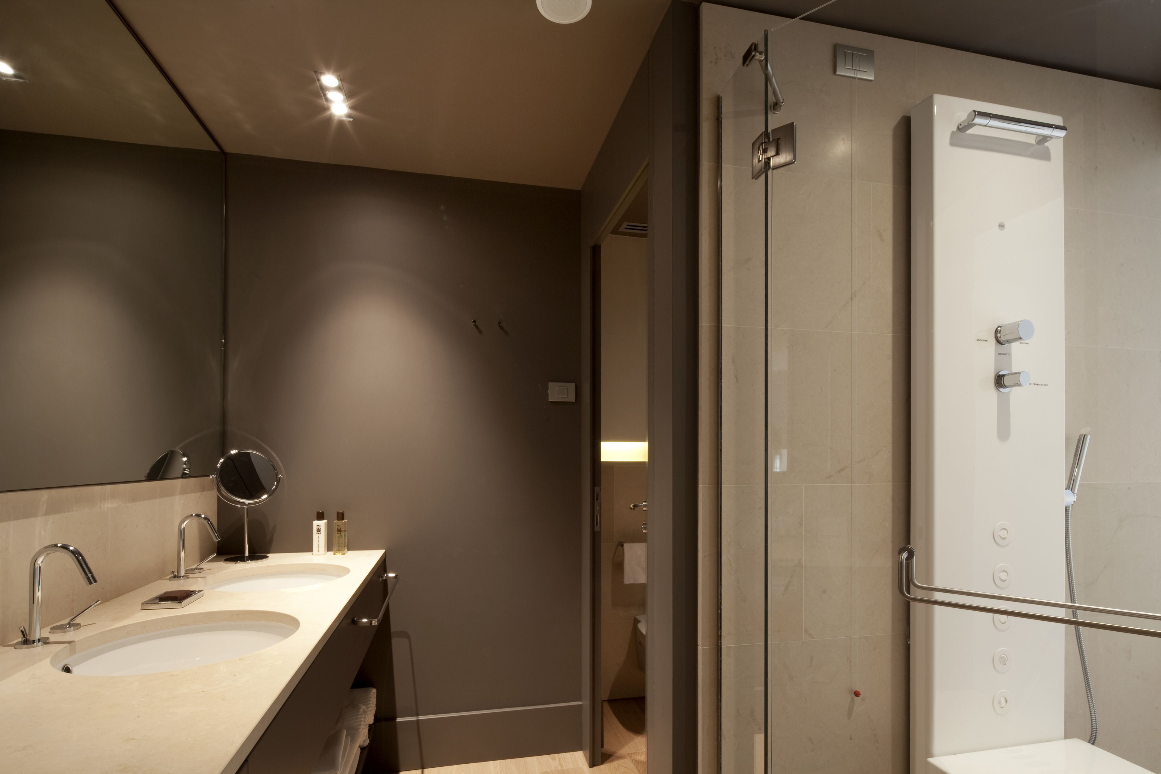 A modern bathroom with two sinks, a large mirror, and a walk-in shower.