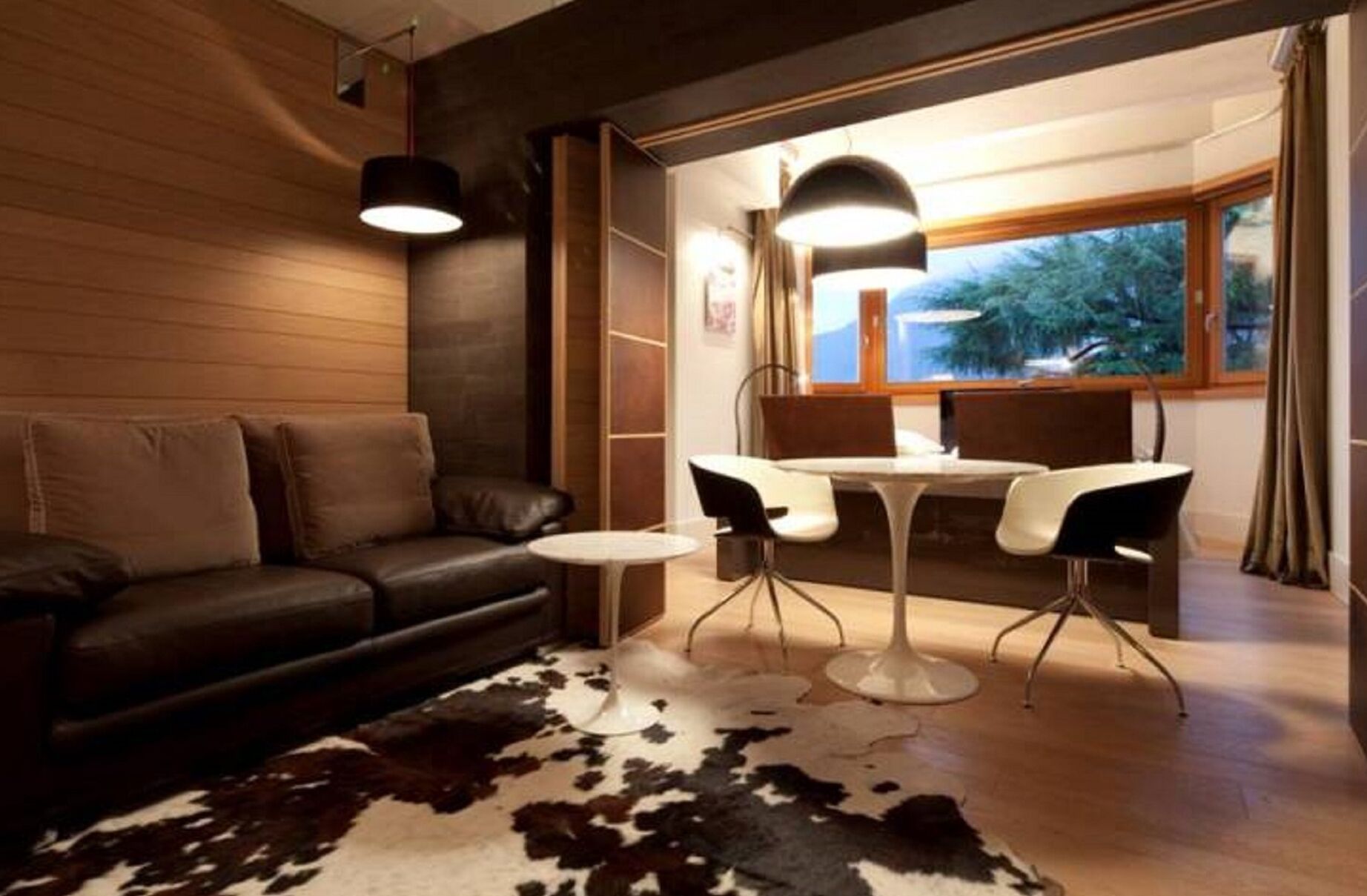 A modern living room with a leather sofa, a round coffee table, and a dining area with a white table and black chairs.