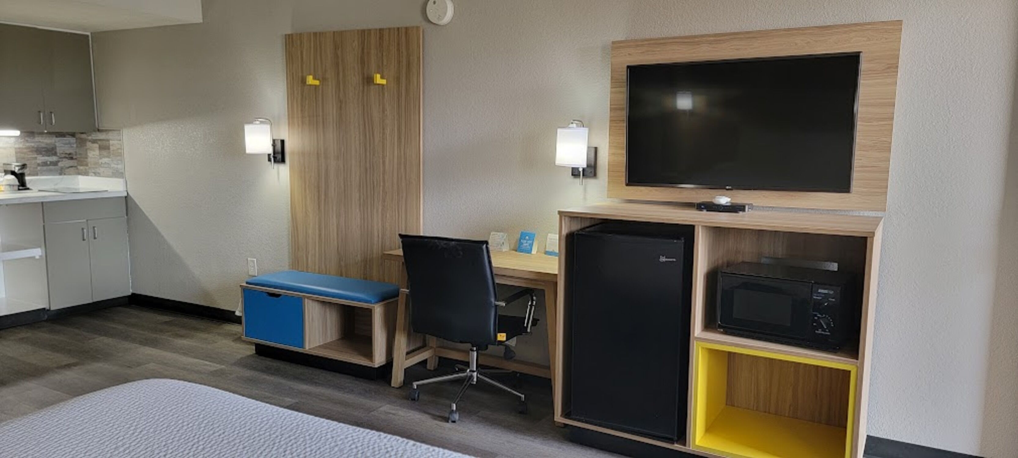 Una habitación de hotel compacta con kitchenette, un escritorio con silla, televisor y microondas.