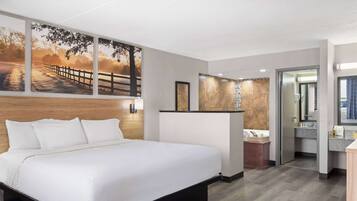 A modern hotel room with a large bed, a bathroom with a sink and mirror, and a view of a sunset through a window.