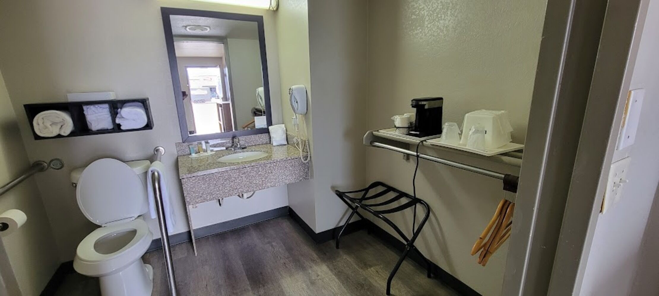 Een badkamer met toilet, wastafel, spiegel, handdoekhouder en een plank met toiletartikelen.