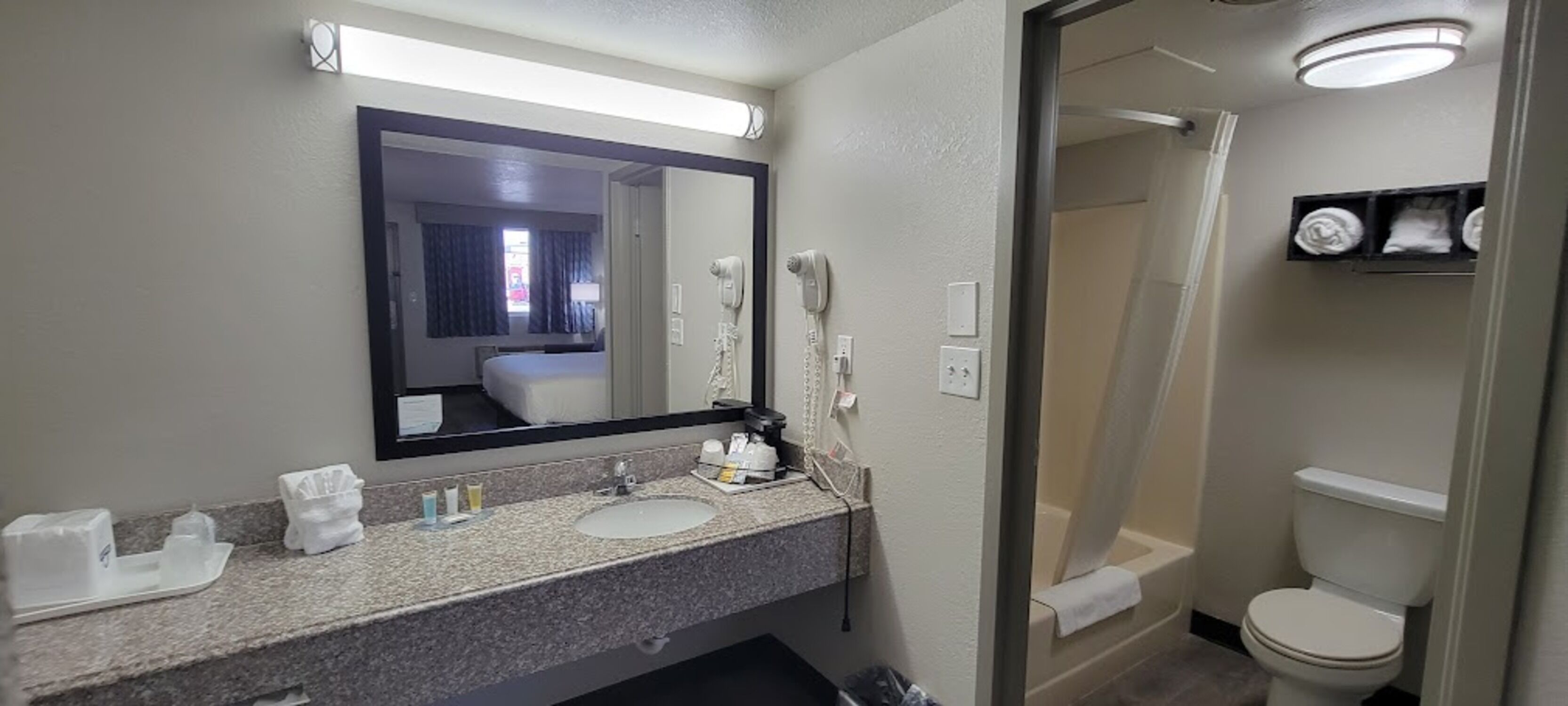 Un baño de hotel con lavamanos doble, un espejo grande, secador de pelo y zona de ducha.