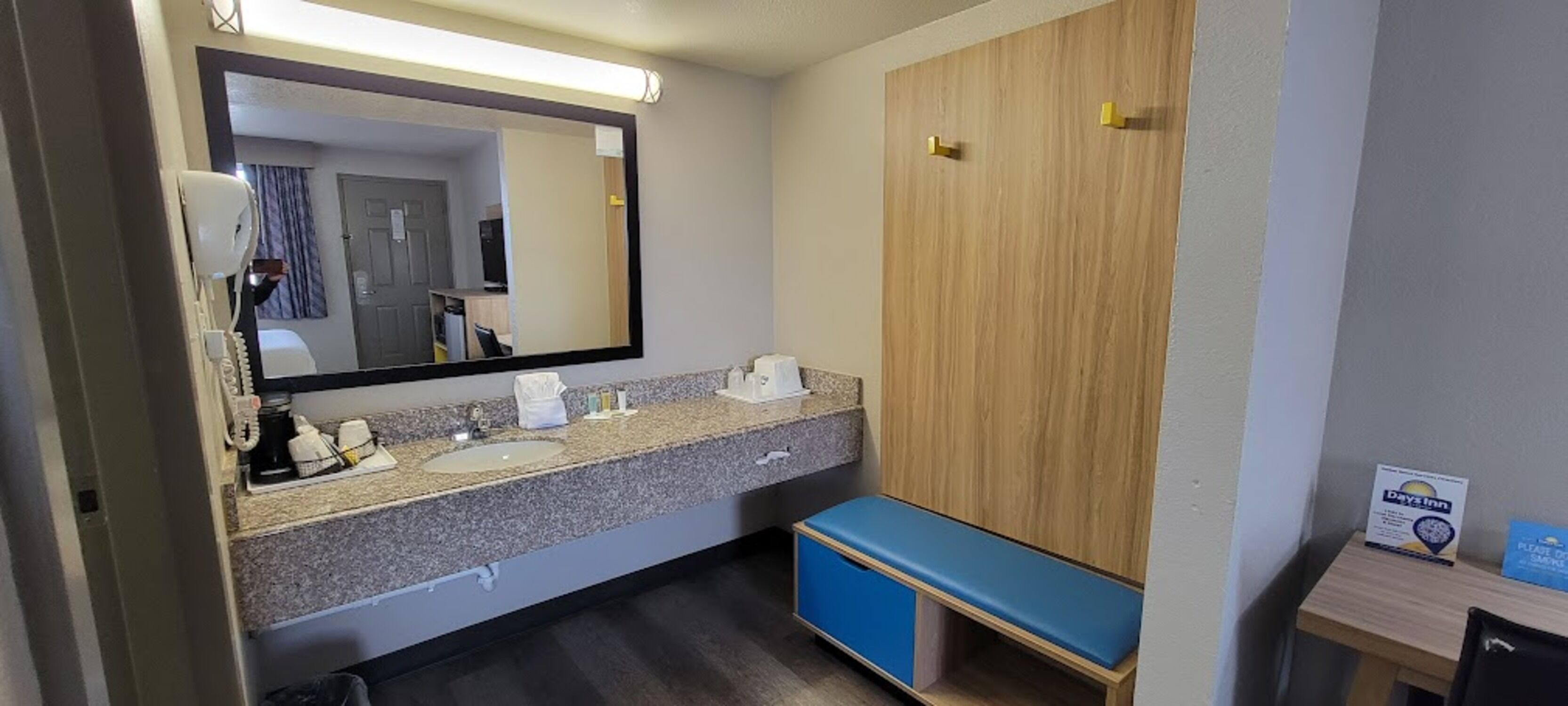 Un baño de hotel con encimera de granito, dos lavamanos, un espejo, un banco azul y un mueble de madera.