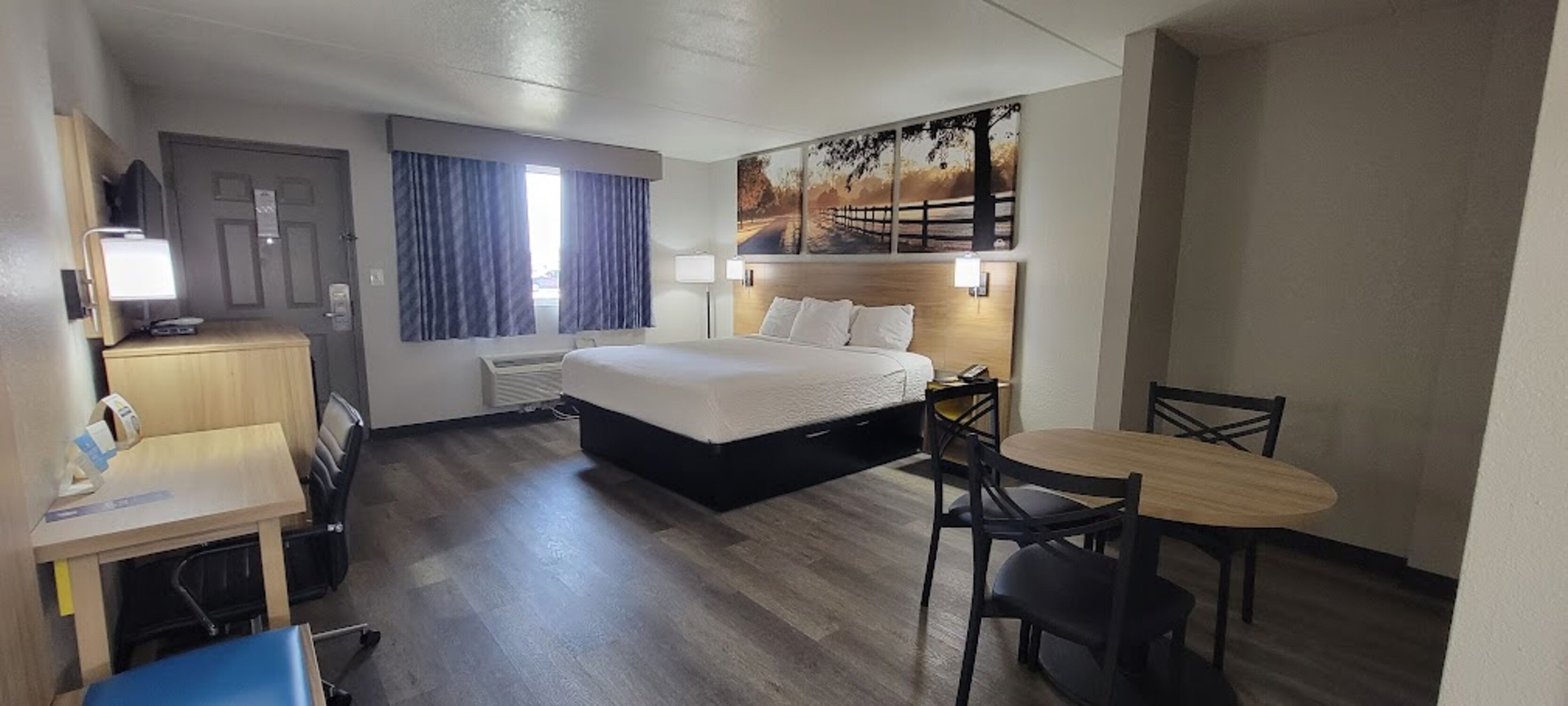 Une chambre d’hôtel avec un lit, un bureau doté d’une lampe, une chaise, une table et un tableau accroché au mur.