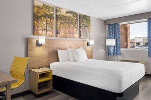 A hotel room with a large bed, a wooden nightstand, a yellow chair, and a window with a view of the street. - Days Inn by Wyndham Conway (Conway)