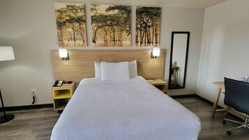Een hotelkamer met een groot bed, een bureau met stoel, een nachtkastje, een lamp en een spiegel.