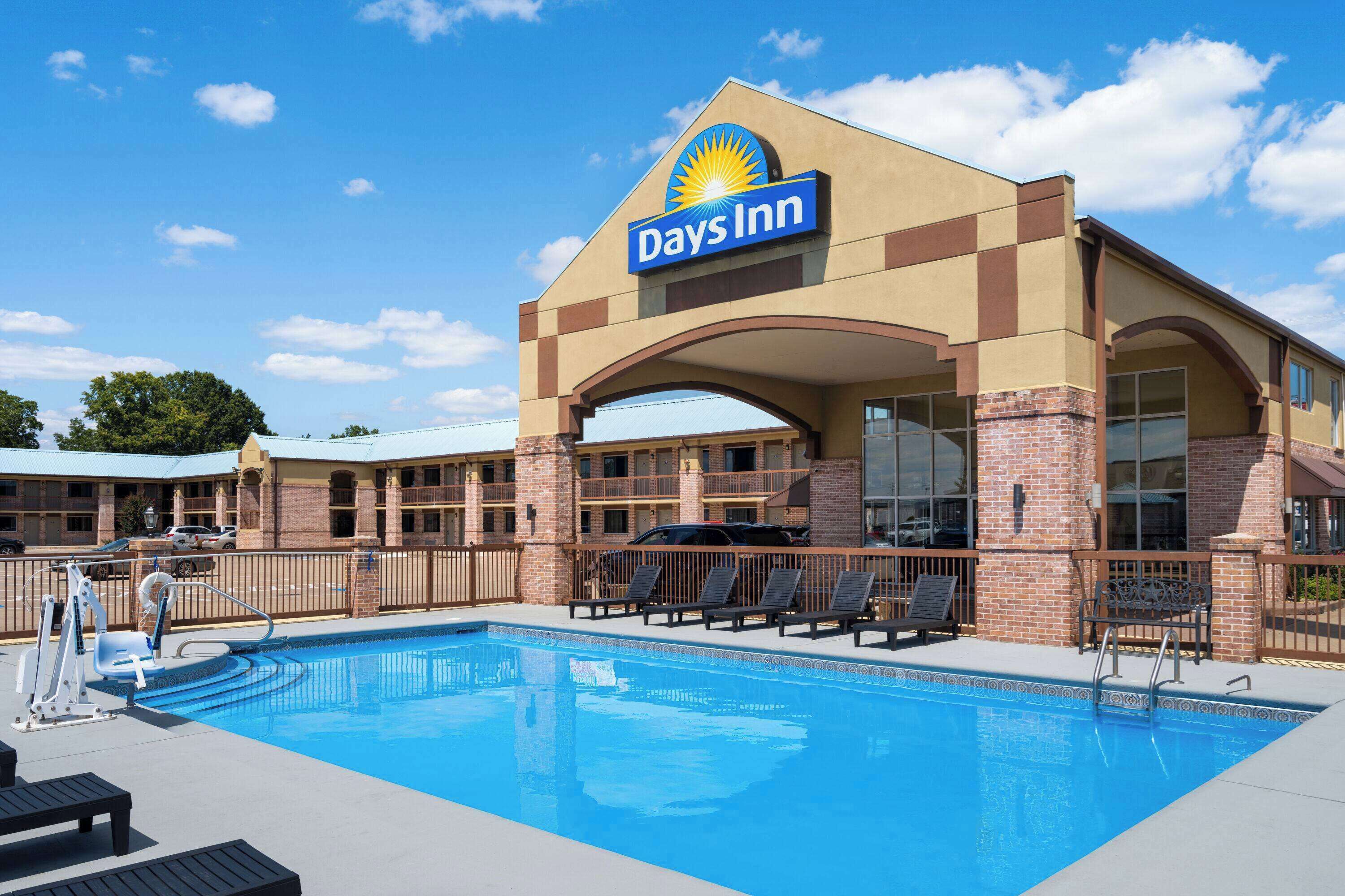 A Days Inn with a swimming pool, outdoor seating, and a clear blue sky.