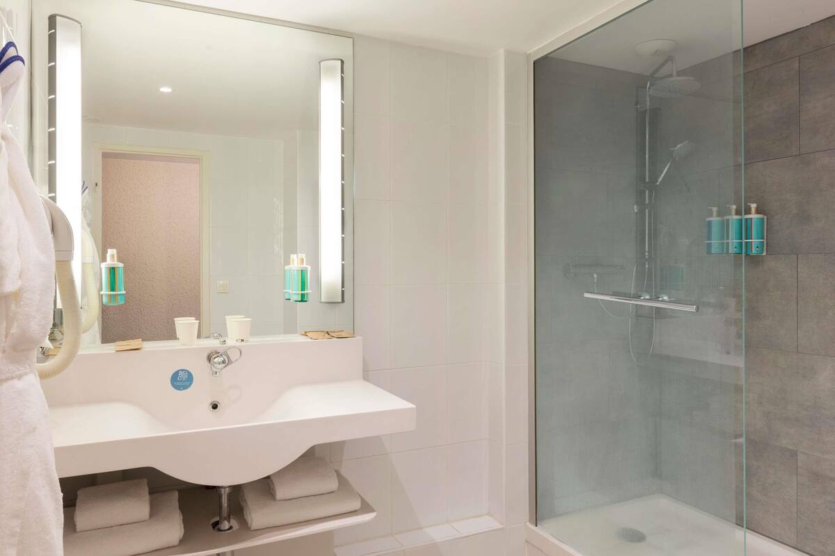 Un baño moderno con cabina de ducha de vidrio, un lavamanos blanco con espejo y artículos de aseo en la encimera.