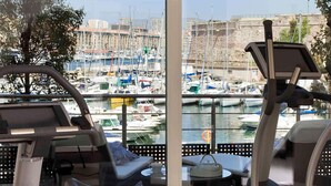 Une salle de sport équipée de matériel d’exercice et offrant une vue sur un port de plaisance avec des bateaux.