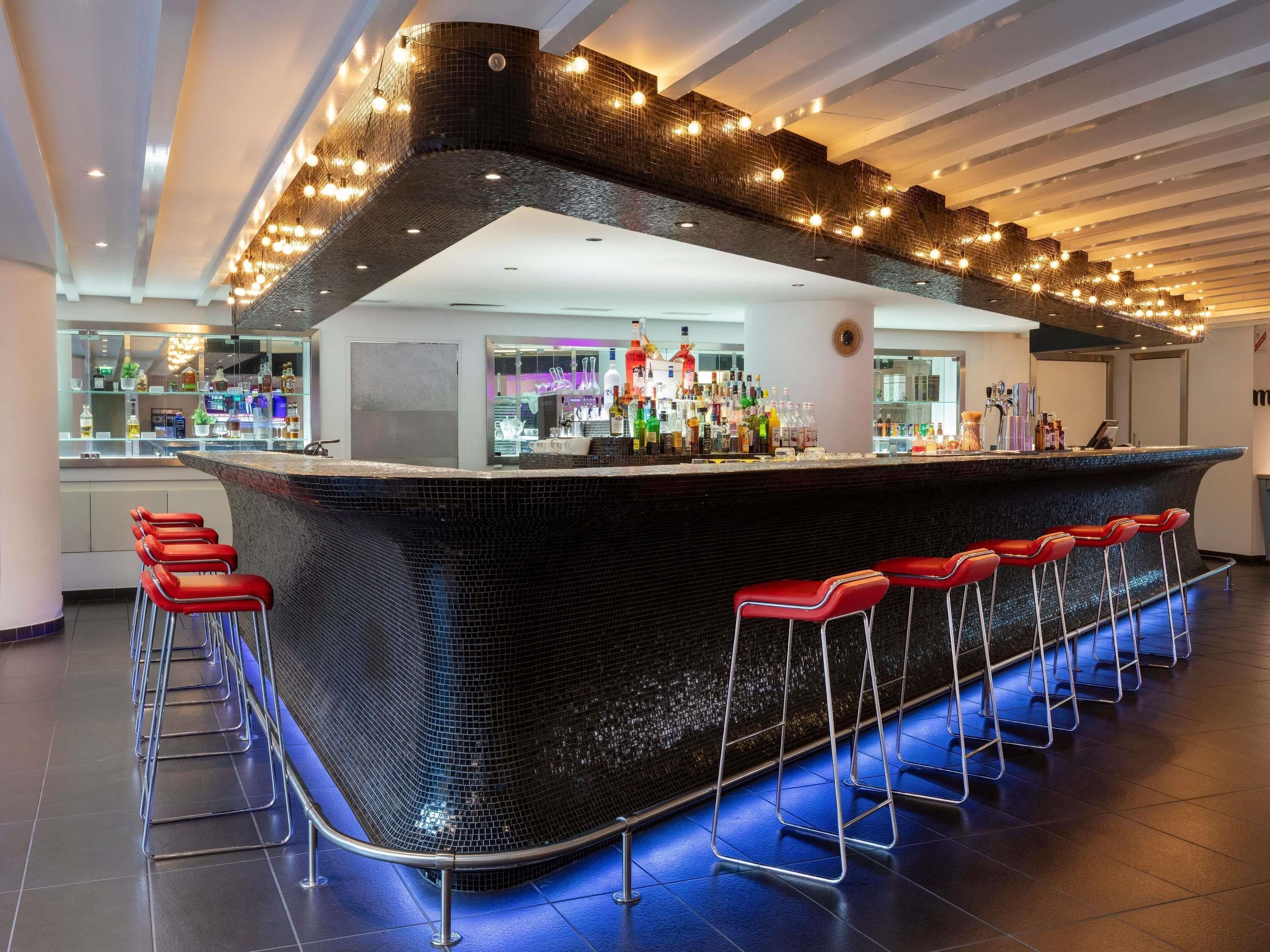 A modern bar area with a curved counter, red bar stools, and a variety of bottles and glasses.