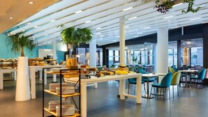 Un café moderne avec des tables blanches, des chaises de couleur turquoise et une variété de produits de boulangerie présentés sur des étagères.
