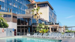 Ein modernes Hotel mit Pool, Liegestühlen und Palmen.