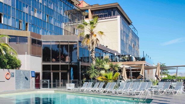 Un hôtel moderne doté d’une piscine, de chaises longues et de palmiers.