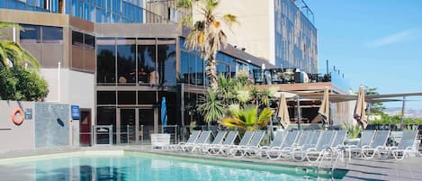 Un hotel moderno con piscina, sillas de descanso y palmeras.