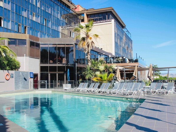 Un hôtel moderne doté d’une piscine, de chaises longues et de palmiers.