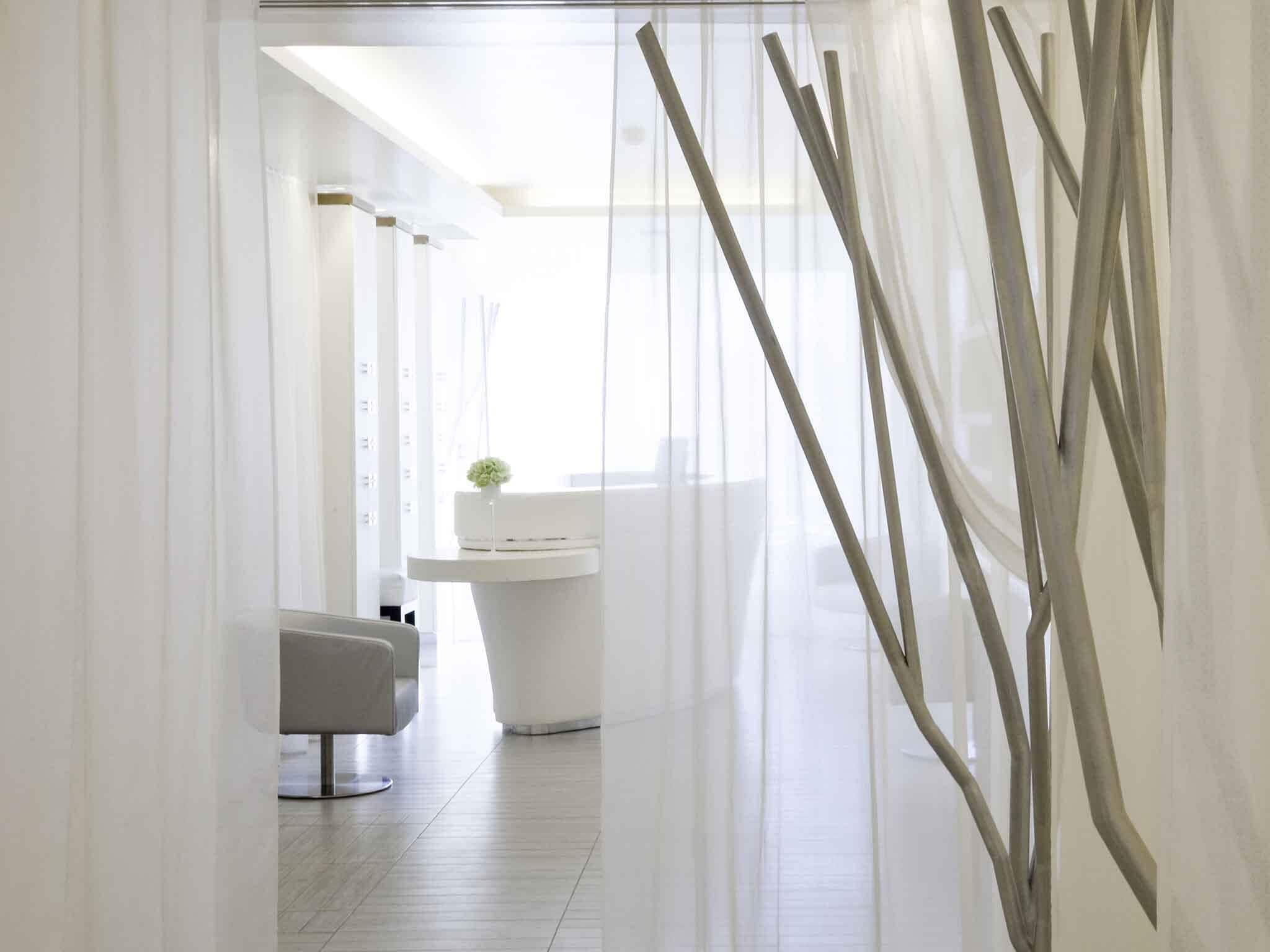 A modern, minimalist bathroom with a white sink, a small plant, and a chair.