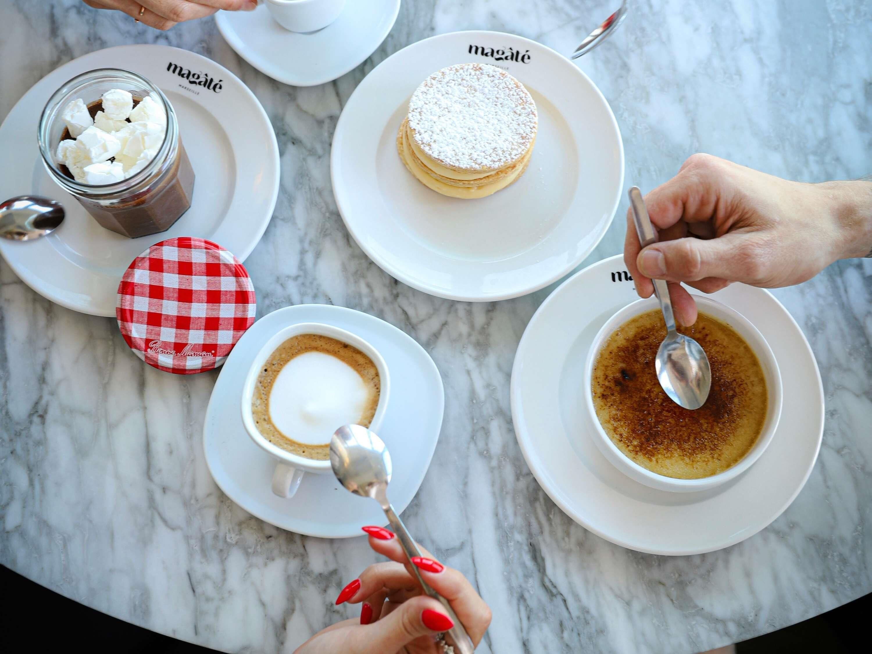 A table with four plates of food and drinks, including a dessert, coffee, and a hot beverage.