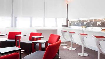 A modern interior with red and black chairs, white bar stools, and a bar counter.