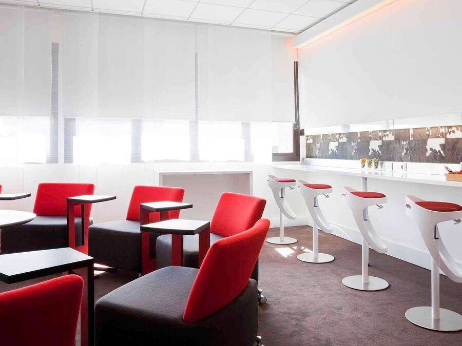 A modern interior with red and black chairs, white bar stools, and a bar counter.
