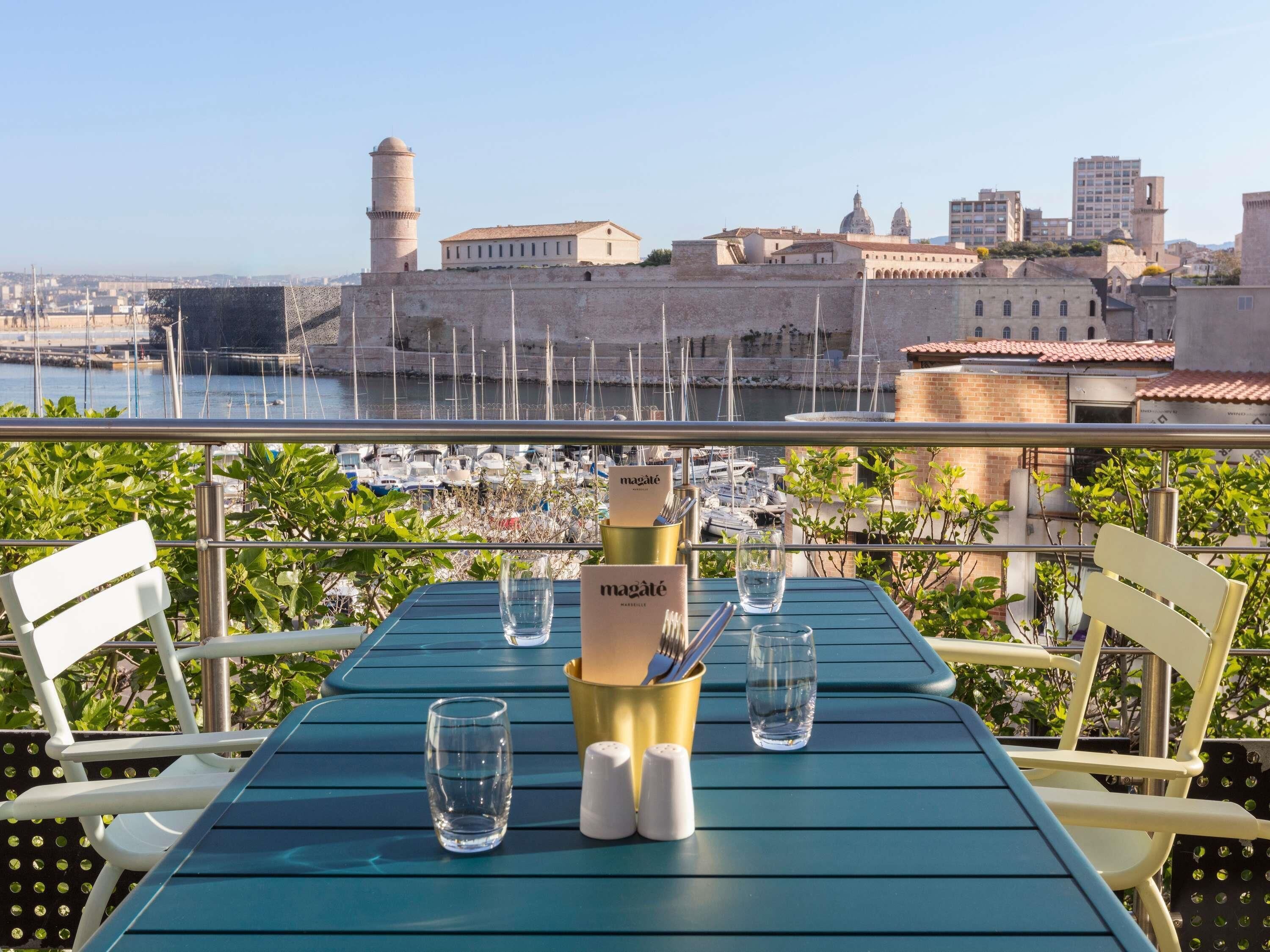 A table with a menu, glasses, and salt shakers on a balcony overlooking a marina and historic buildings.