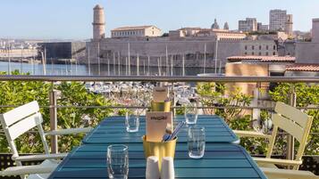 Una mesa con un menú, vasos y saleros en un balcón con vistas a un puerto deportivo y edificios históricos.