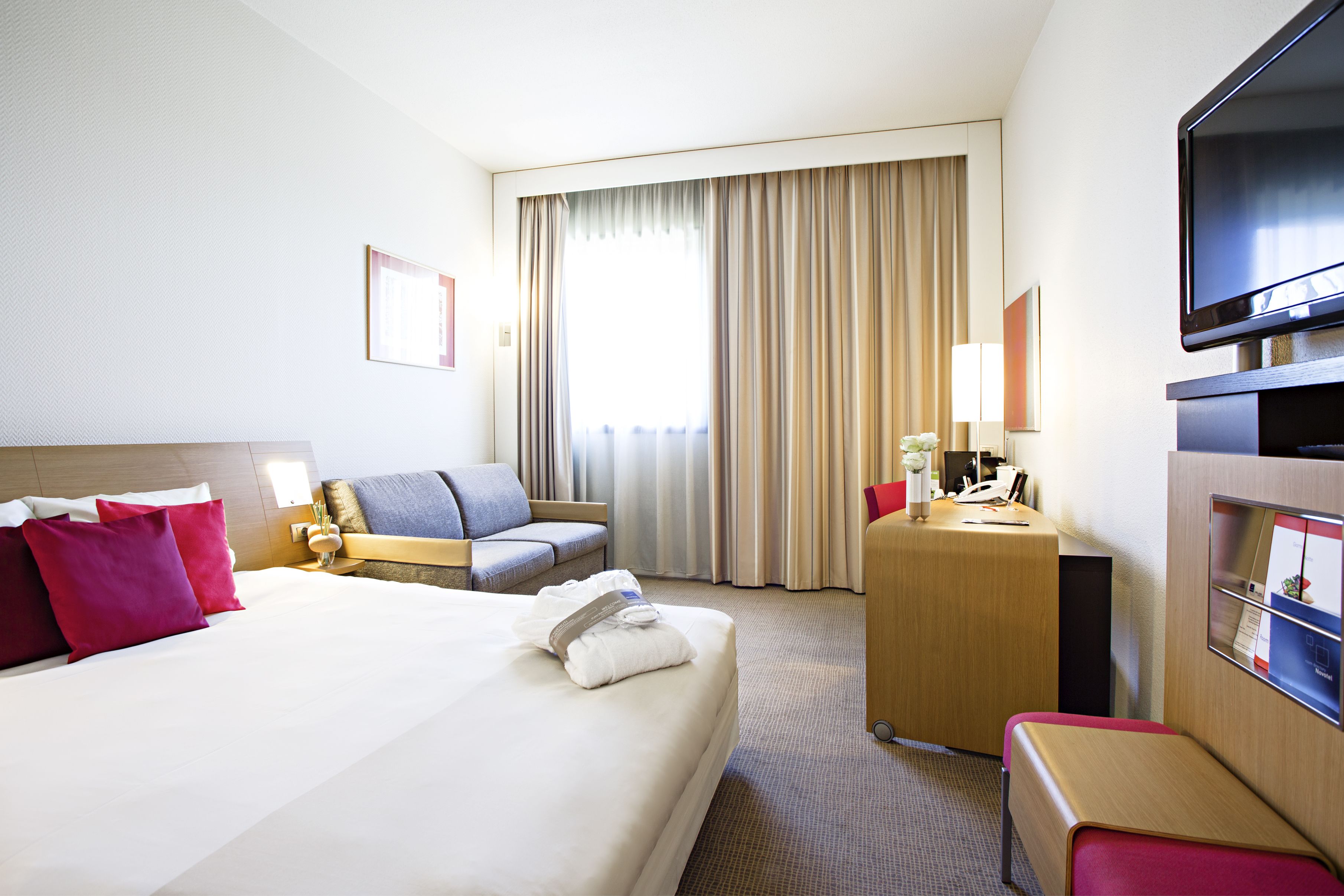 A hotel room with a large bed, a desk, a chair, a TV, and a window with curtains.