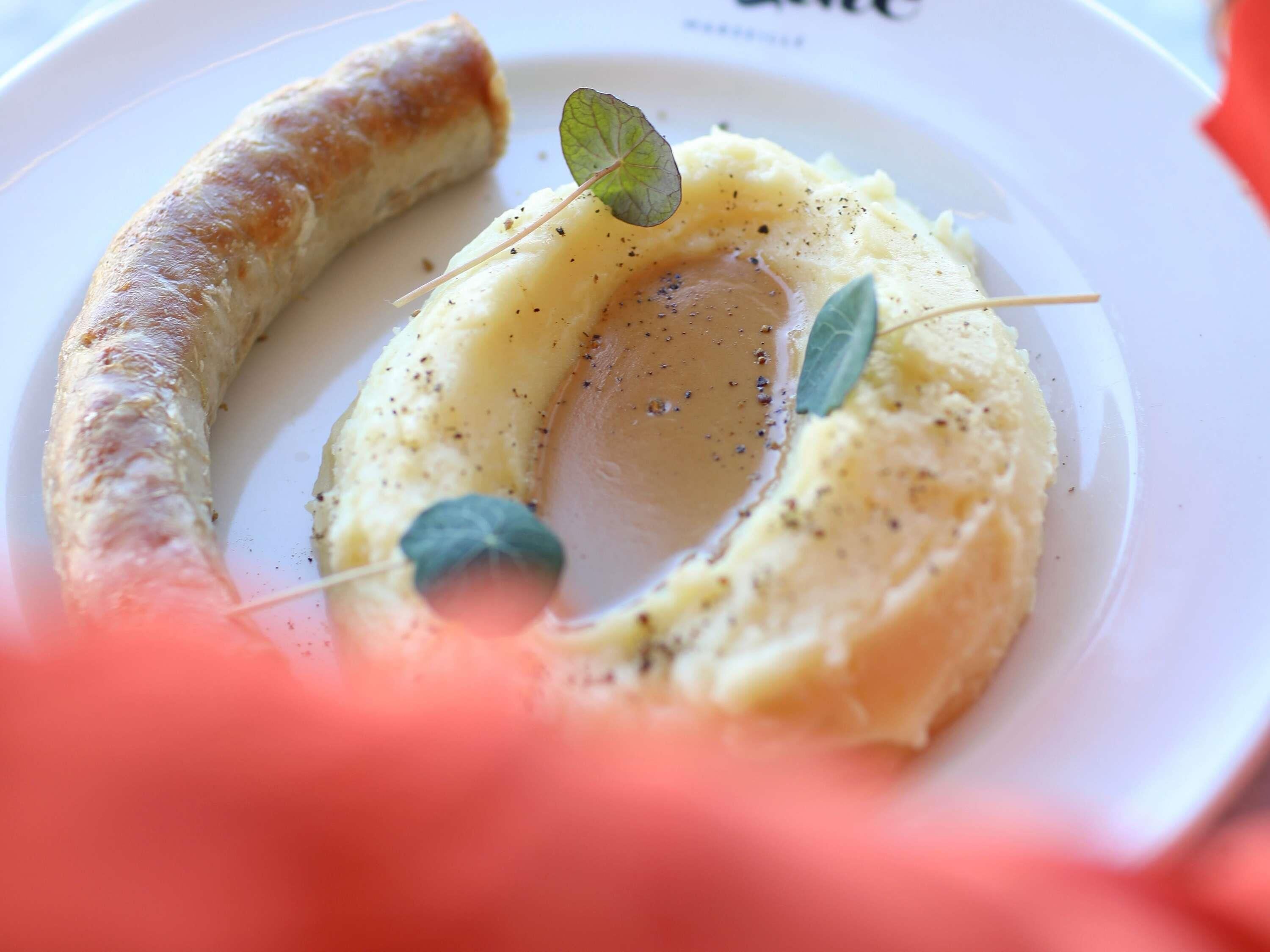 A plate with mashed potatoes, a sausage, and a garnish.