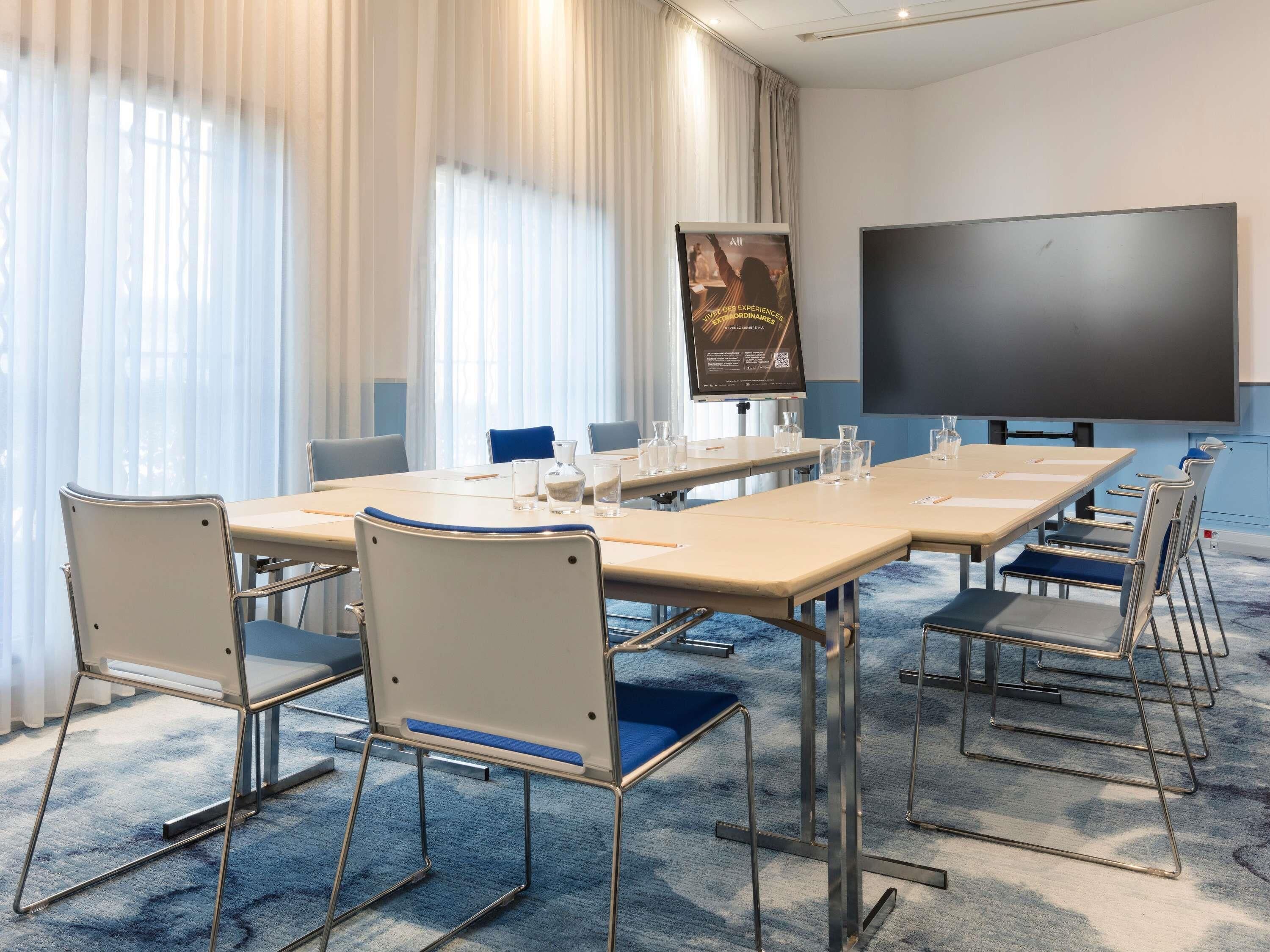 A conference room with a large table, chairs, a projector screen, and a poster on the wall.